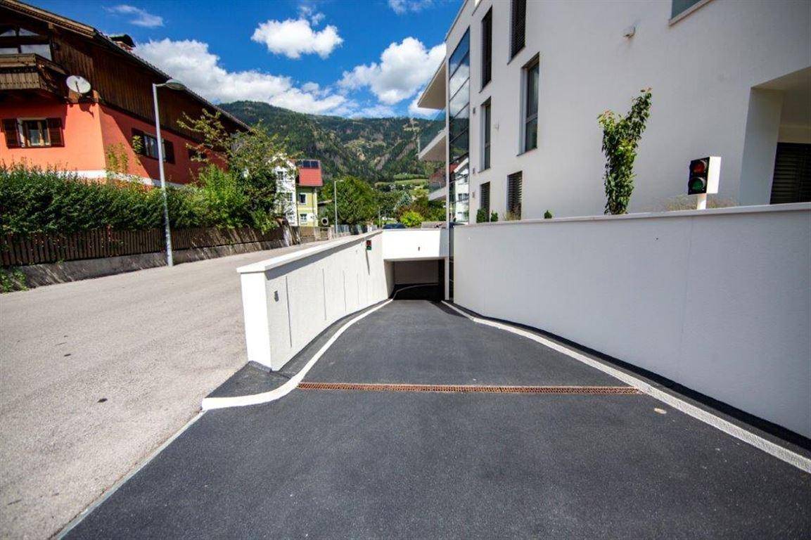 Zufahrt zur Tiefgarage eines modernen Wohnkomplexes mit Bergkulisse im Hintergrund.
