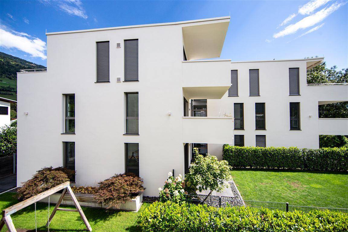 Moderne Wohnanlage mit weißer Fassade, großen Fenstern und gepflegter Grünfläche.