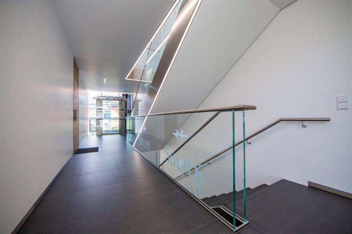 Moderner Treppenaufgang mit Glasgeländer, Edelstahlhandlauf und heller Beleuchtung.