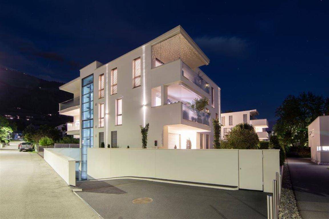 Elegantes Mehrfamilienhaus bei Nacht mit moderner Architektur und beleuchteten Balkonen.