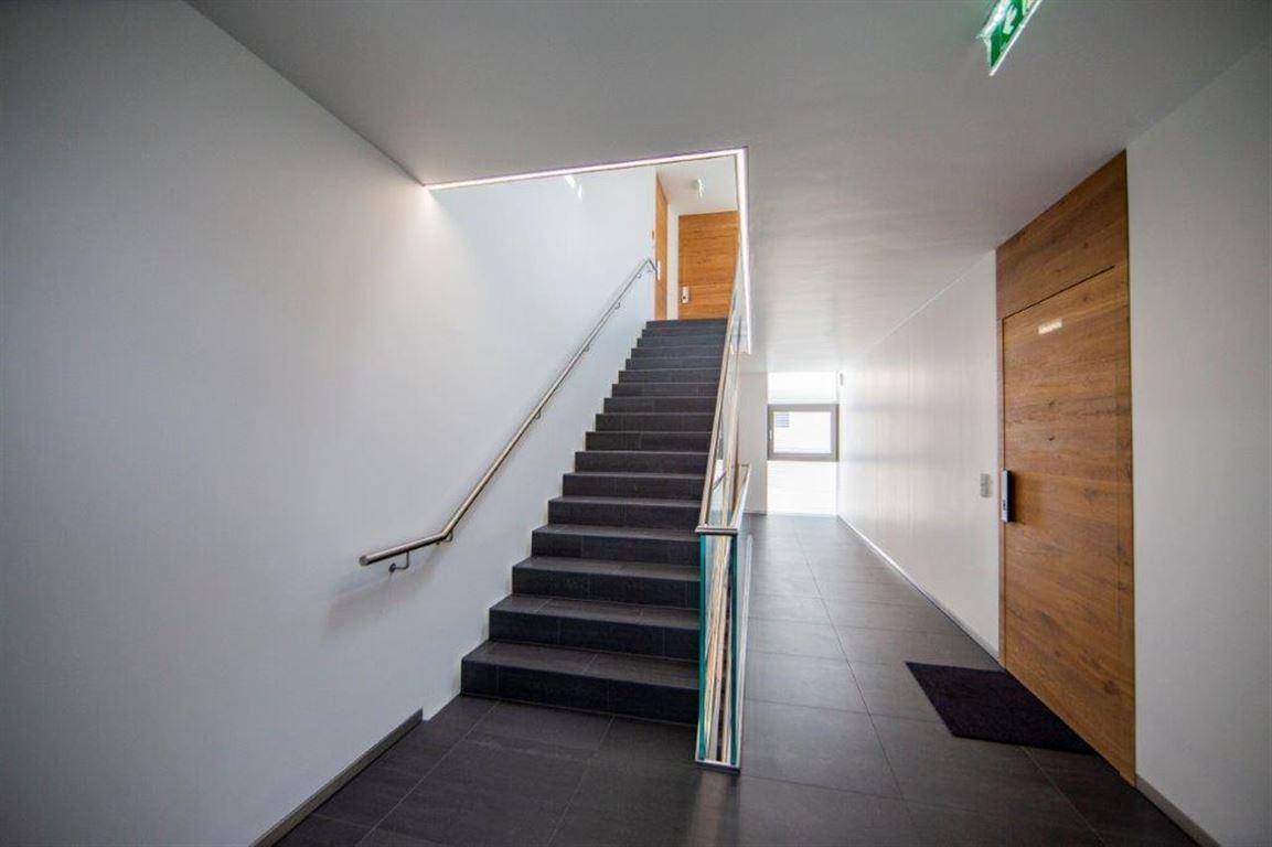 Helles Treppenhaus mit modernen Stufen, Edelstahlgeländer und großformatigen Fliesen.