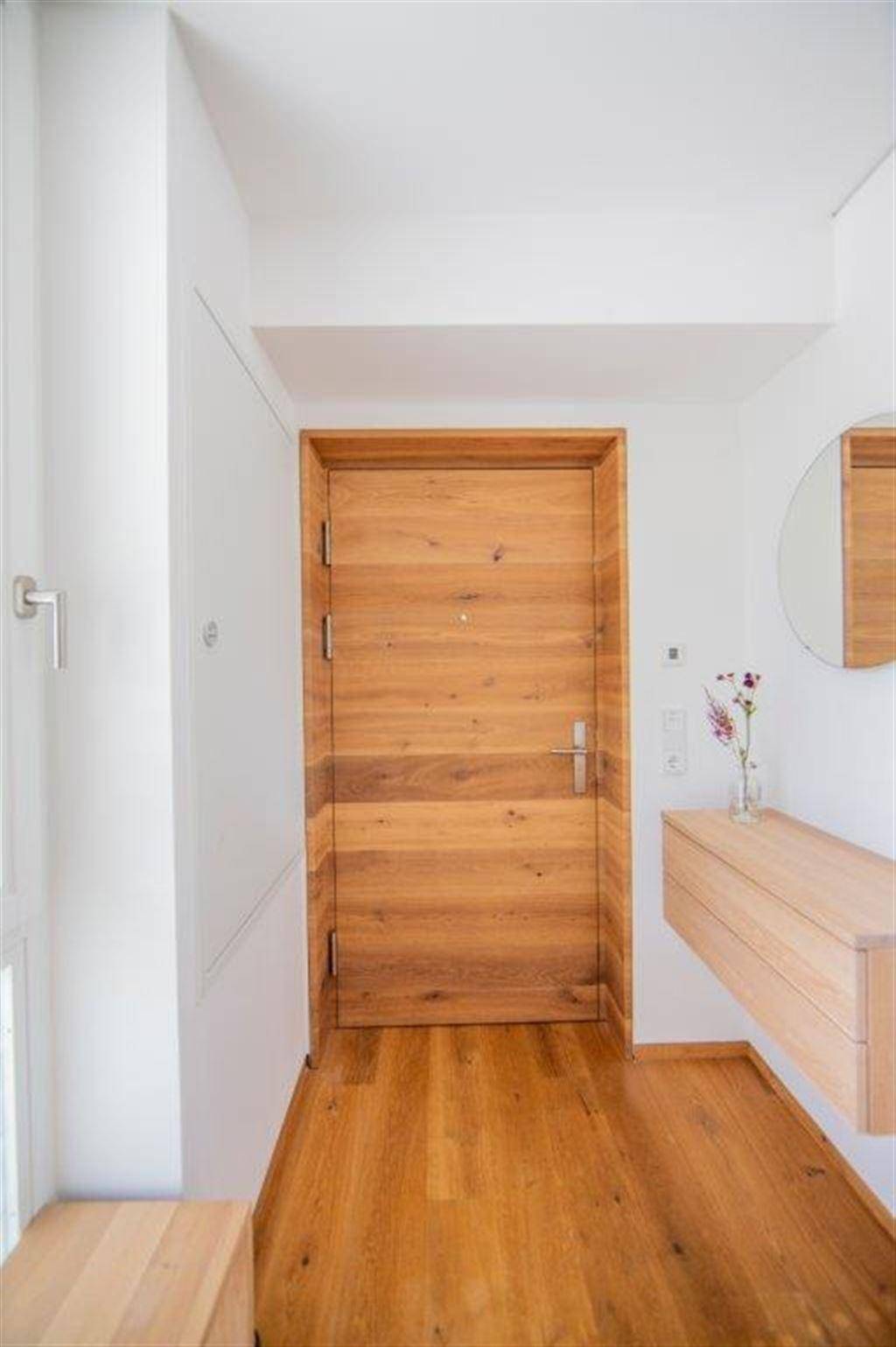 Heller Flur mit Holzboden und einer modernen Holztür, die zu einer Wohnung führt.