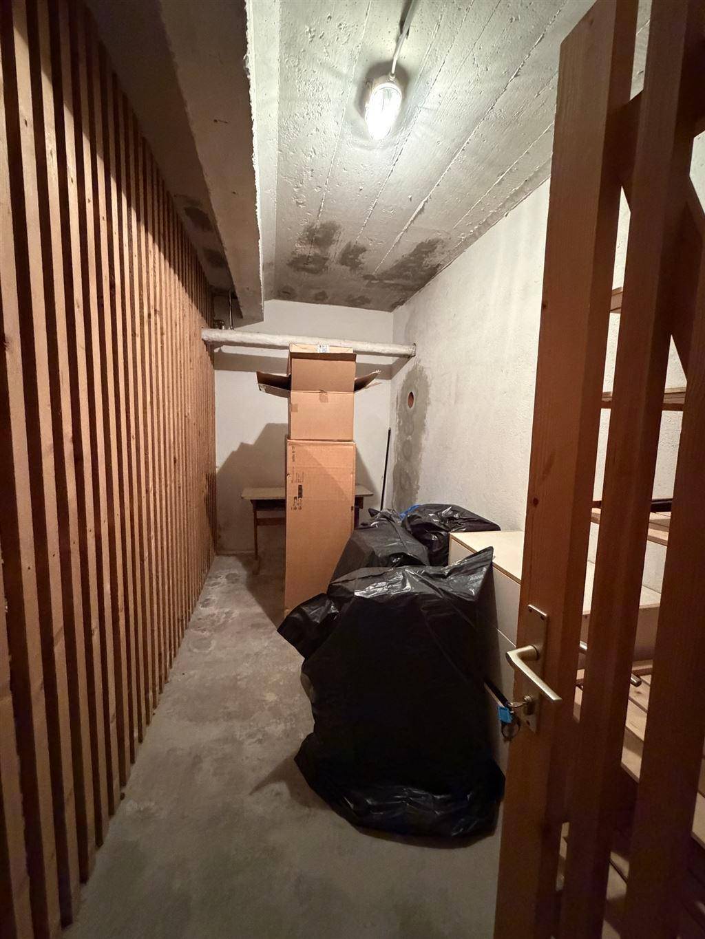 Einfacher Abstellraum mit Holzverkleidung an einer Wand und Betonboden.