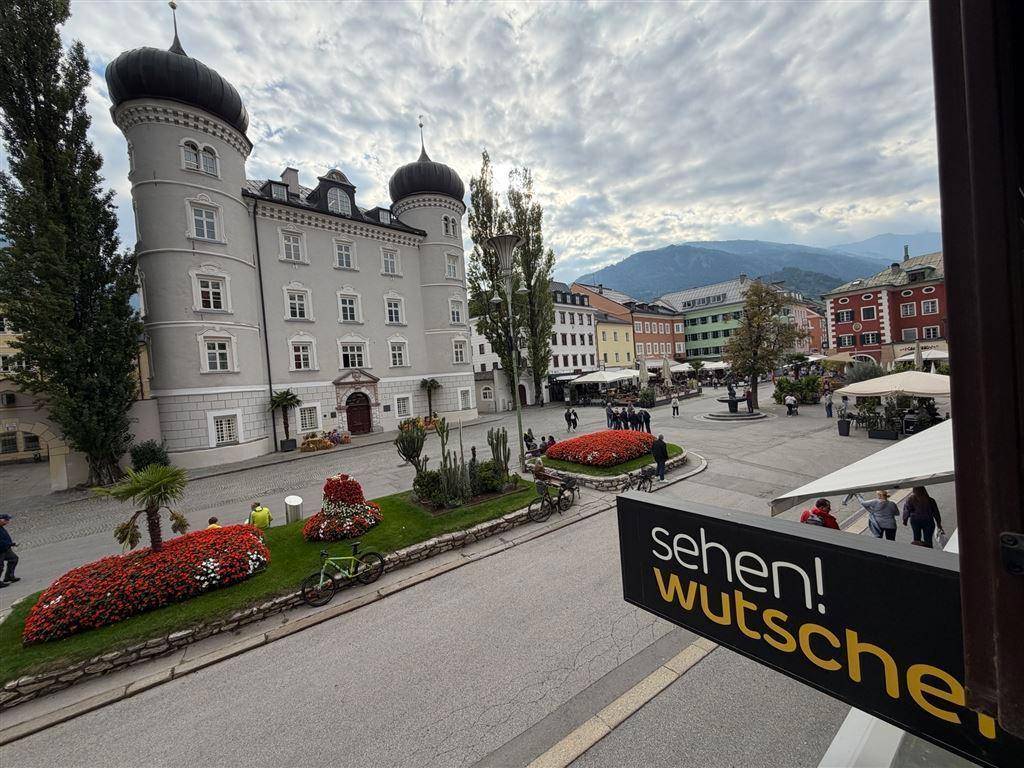 Historischer Stadtplatz mit Schloss, bunten Gebäuden und blühenden Blumenbeeten.