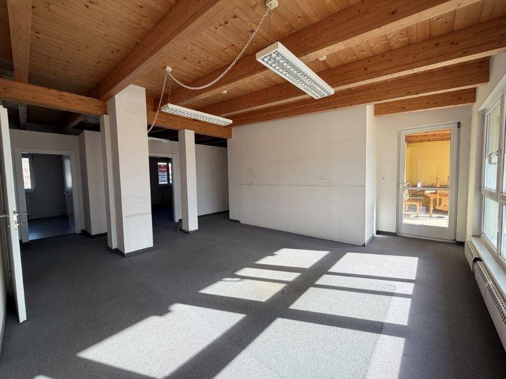 Geräumiger Büroraum mit Holzbalkendecke, grauem Teppichboden und viel Tageslicht, mit Bergblick.
