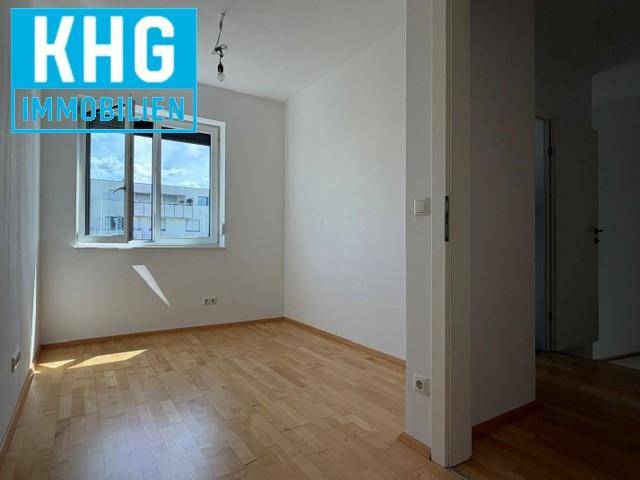 Geräumiges, unmöbliertes Zimmer mit hellem Holzboden und einem großen Fenster.