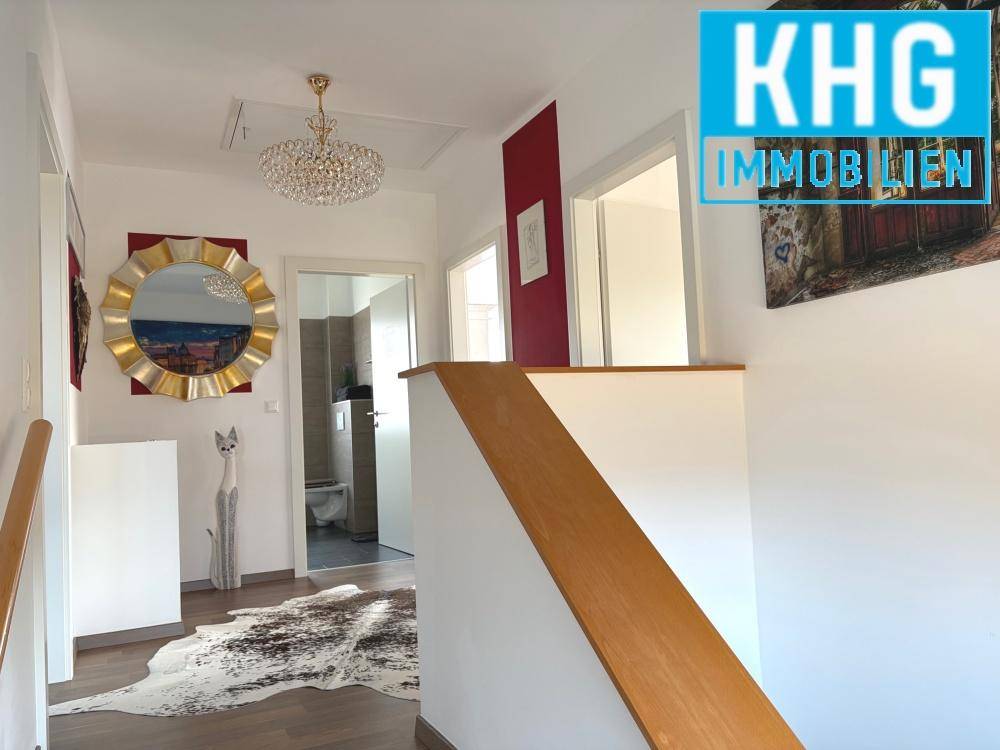 Heller Flur im Obergeschoss mit Treppe, Parkettboden und dekorativem Spiegel.