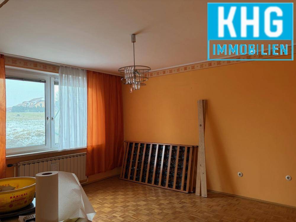 Geräumiges Zimmer mit orangefarbenen Wänden, Parkettboden und großem Fenster.