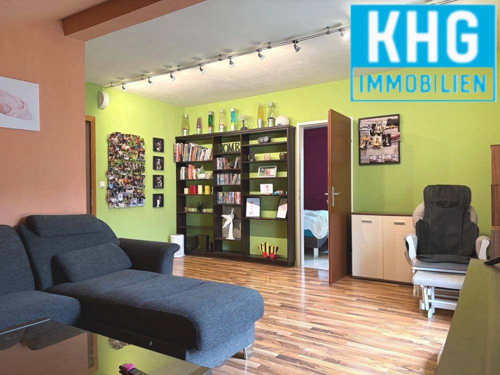 Geräumiges Wohnzimmer mit Holzboden, Bücherregal und farbenfroher Wandgestaltung.
