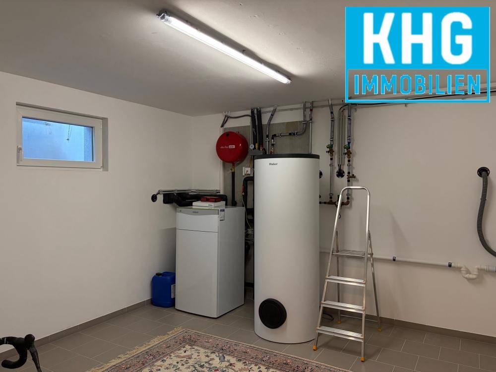 Technikraum im Keller mit Heizungsanlage, Warmwasserspeicher und kleinem Fenster.
