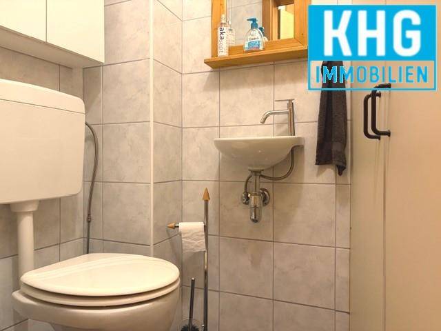 Kleines Gäste-WC mit Wand-WC, Waschbecken und hellen Fliesen.