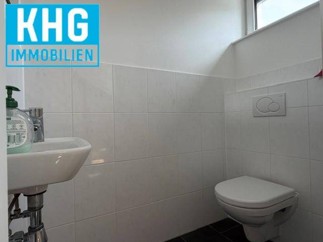 Kleines Gäste-WC mit weißen Fliesen, wandhängendem WC und einem einzelnen Waschbecken.