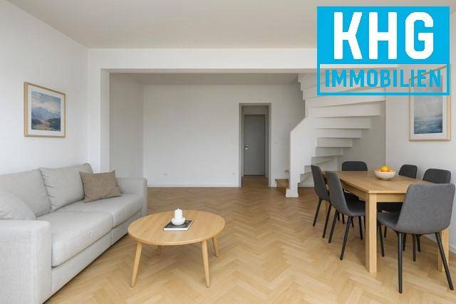 Gemütlicher Wohn- und Essbereich mit Parkettboden, Sofa und Esstisch, verbunden durch eine offene Treppe.