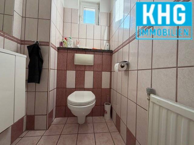 Separate Toilette mit Wand-WC und Fliesen in zwei Farbtönen.
