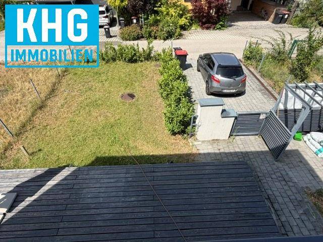 Geräumige Holzterrasse grenzt an einen kleinen Rasenbereich und eine gepflasterte Einfahrt.