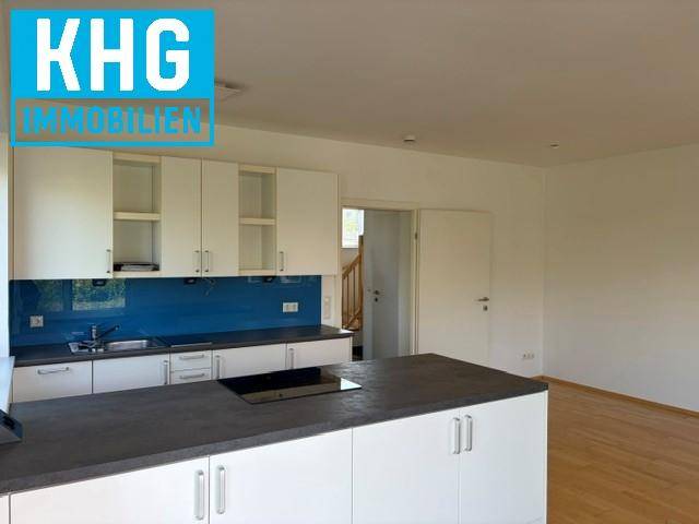 Moderne Küche mit weißen Schränken, dunkler Arbeitsplatte, blauer Rückwand und Kochinsel.