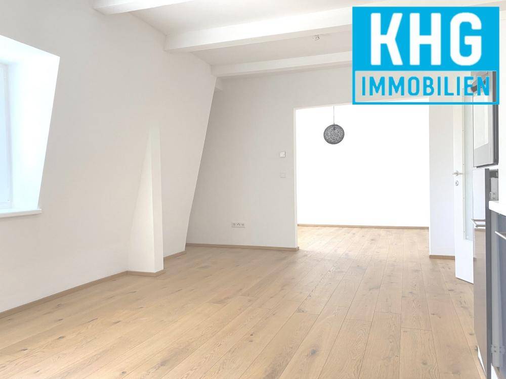 Geräumiger offener Wohnbereich mit Holzboden, weißen Wänden und sichtbaren Deckenbalken.