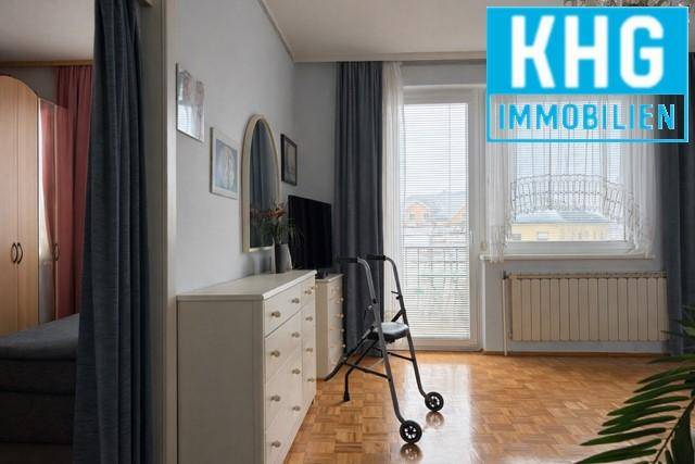 Schlafzimmer mit Parkettboden, Kommode und Zugang zu einem Balkon.