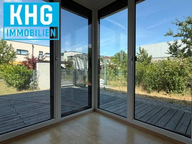 Lichtdurchfluteter Innenraum mit großen Glasfronten und direktem Zugang zu einer Holzterrasse.
