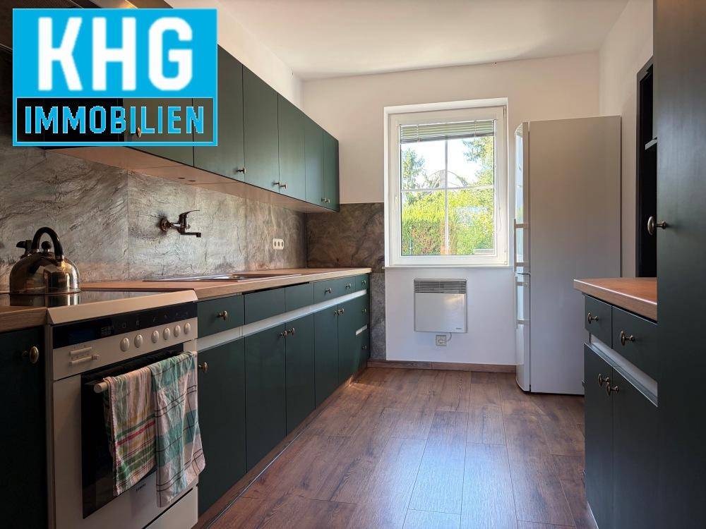 Küche mit dunkelgrünen Schränken, Holzarbeitsplatten und Fensterblick ins Grüne.