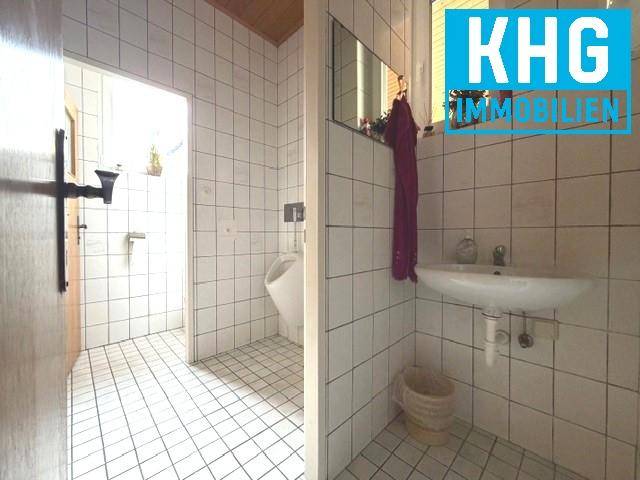 Gefliester Toilettenraum mit Urinal, Waschbecken und weißem Fliesenboden.