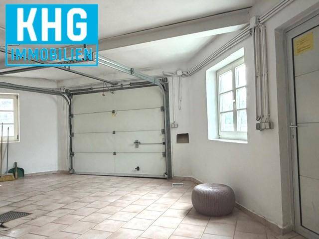 Geräumige Garage mit Fliesenboden und Fenstern, bietet Platz für Fahrzeuge und Lagerung.