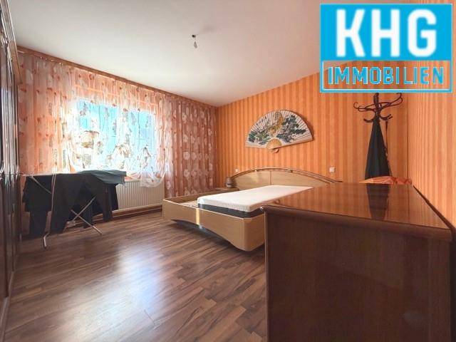 Schlafzimmer mit Bett, Kleiderschrank und gemusterten Tapeten.