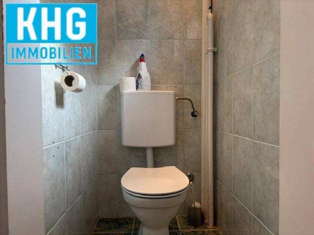 Kleines WC mit Toilette und grauen Wandfliesen.