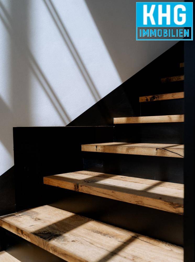 Nahaufnahme einer Holztreppe mit schwarzen Stufen, die durch das einfallende Licht betont wird.