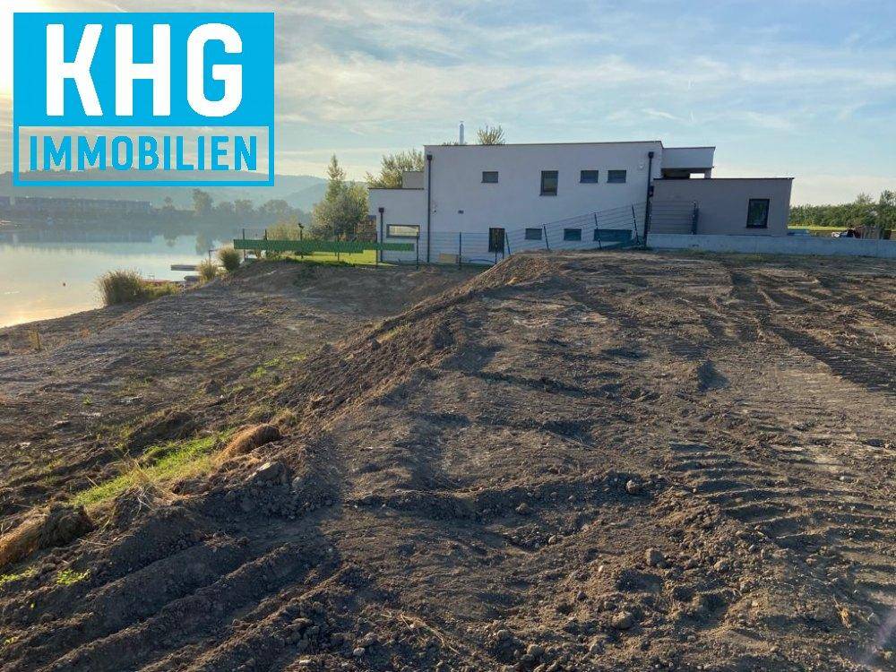 Unbebautes Grundstück am Seeufer neben einem modernen Haus mit Blick auf das Wasser.