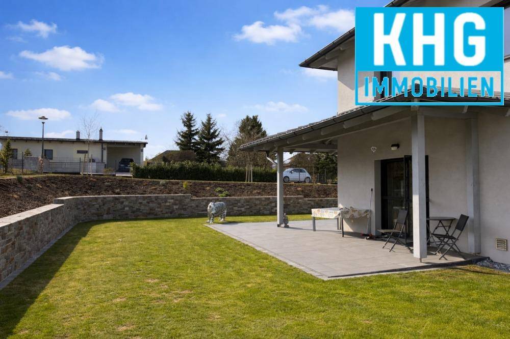 Seitlicher Blick auf das Einfamilienhaus mit Terrasse, Rasenfläche und Steinmauer im Garten.