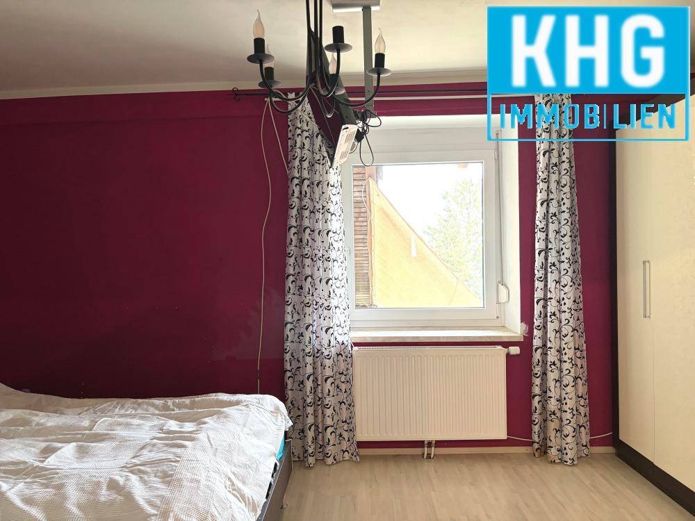 Schlafzimmer mit Holzboden, Fenster und dunkler Wandfarbe, gemütlich eingerichtet.