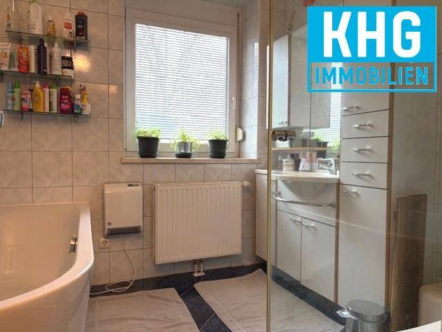 Helles Badezimmer mit Badewanne, Fenster und weißen Fliesen, ausgestattet mit Heizkörper.