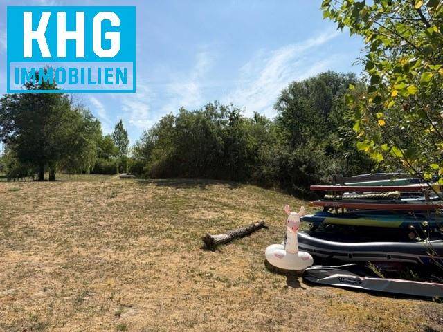 Weitläufige Grünfläche mit Bäumen und gestapelten Wassersportgeräten am Rande des Geländes.