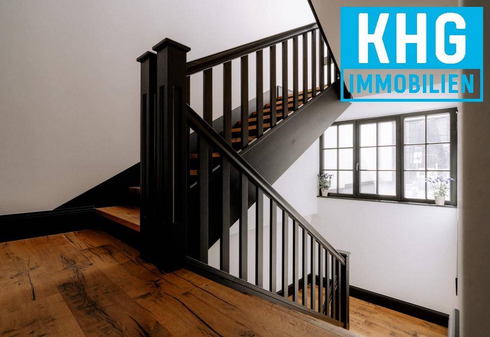 Elegante Holztreppe mit schwarzem Geländer und großen Fenstern, die viel Licht hereinlassen.