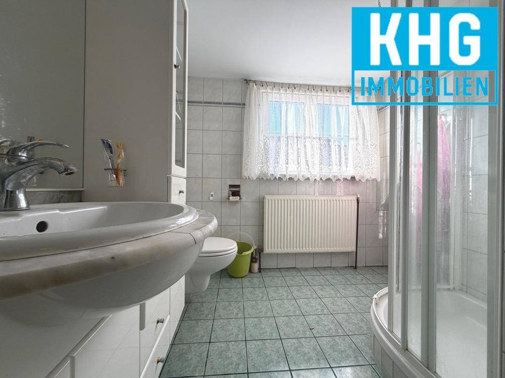 Badezimmer mit Duschkabine, Fenster und hellen Fliesen.