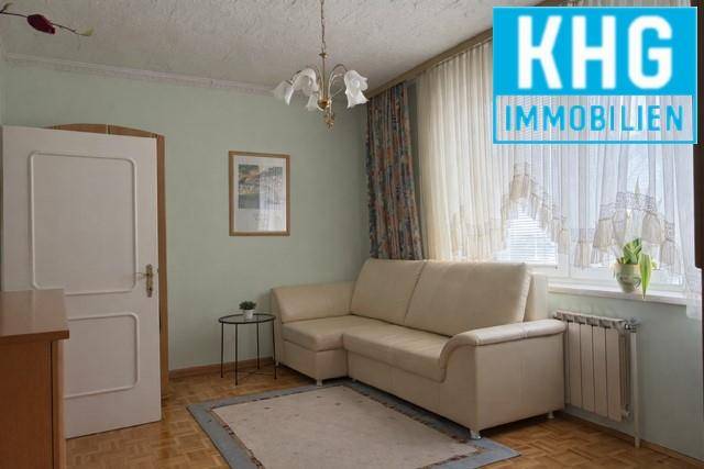 Gemütliches Wohnzimmer mit hellem Sofa, Fenster und Heizkörper.
