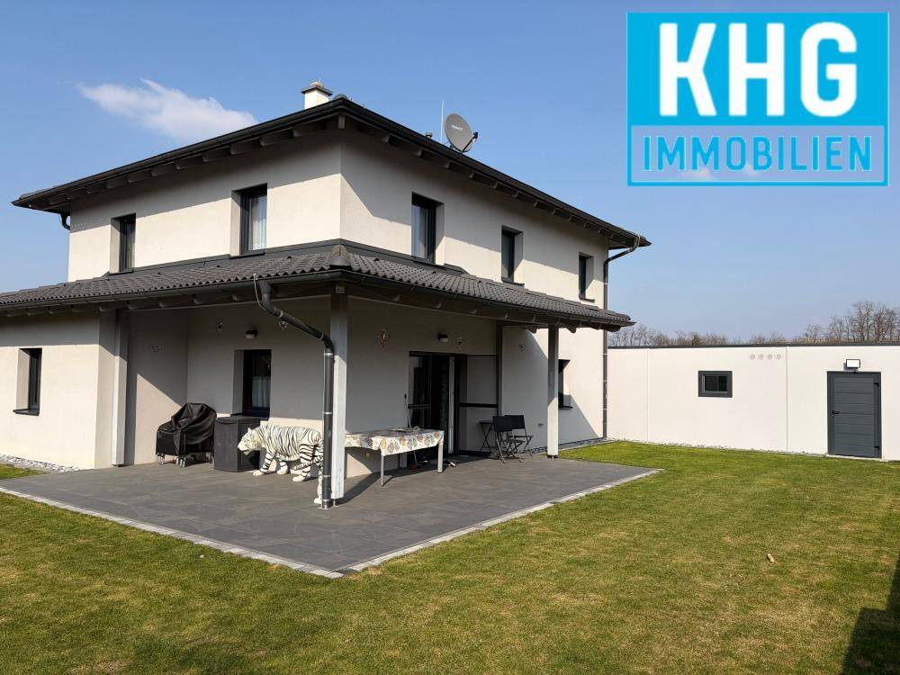 Modernes Einfamilienhaus mit großer Rasenfläche und gepflasterter Terrasse an einem sonnigen Tag.