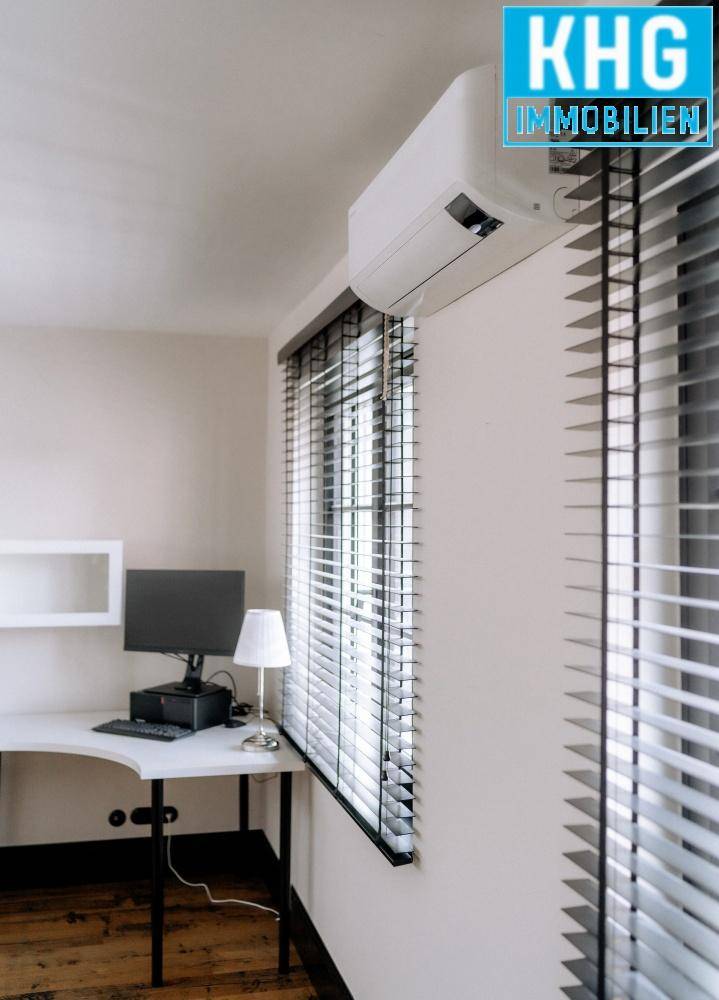 Heller Bürobereich mit Schreibtisch, Computer und Klimaanlage über dem Fenster.