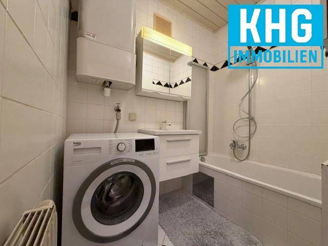 Badezimmer mit Badewanne, Waschmaschine und weißen Fliesen an Wänden und Boden.