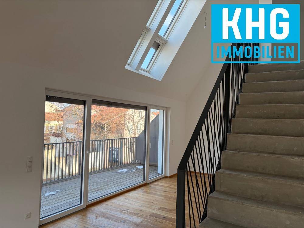 Heller Eingangsbereich mit Holztreppe und Zugang zu einem Balkon, beleuchtet durch Dachfenster.