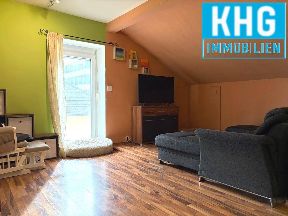 Gemütliches Wohnzimmer im Dachgeschoss mit Schräge, Holzboden und Zugang zum Balkon.