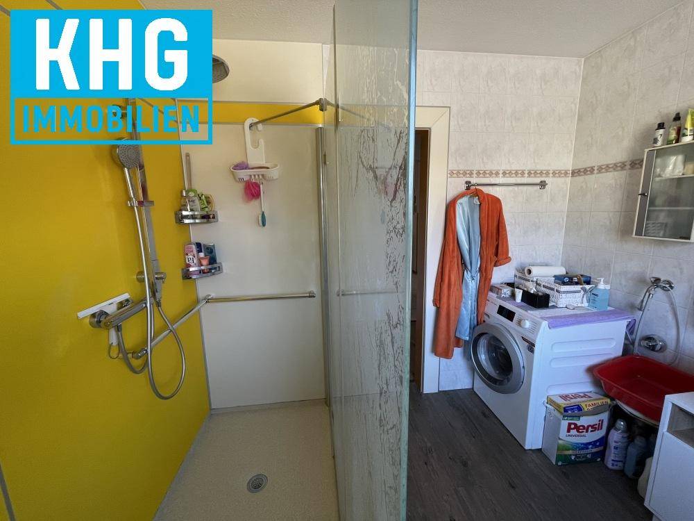 Badezimmer mit ebenerdiger Dusche, Waschmaschine und hellen Fliesen, funktional gestaltet.