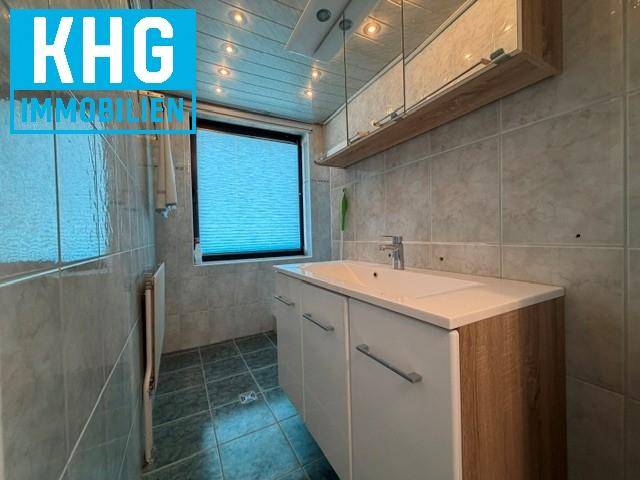 Badezimmer mit grauen Fliesen, Einzelwaschbecken und Holzdeckenverkleidung.