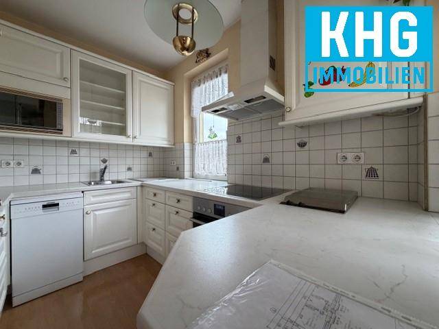 Helle Küche mit weißen Einbauschränken, Fliesenrückwand und Fenster.