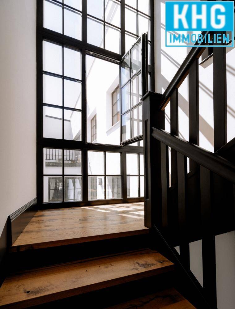 Helle Treppe mit Holzdielen und schwarzem Geländer neben einer großen Fensterfront.