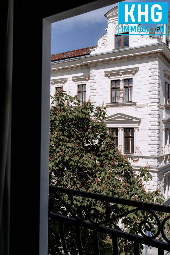 Historische Fassade eines Gebäudes mit verzierten Fenstern, gesehen durch ein Fenster mit Geländer.