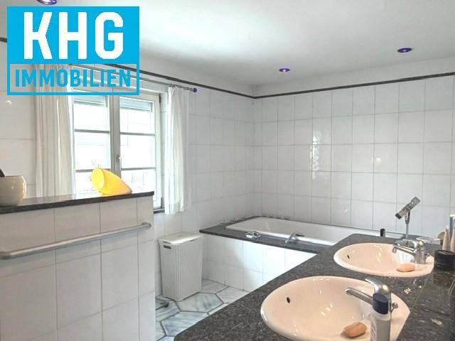 Geräumiges Badezimmer mit Badewanne, Doppelwaschbecken und Fenster, hell gefliest.