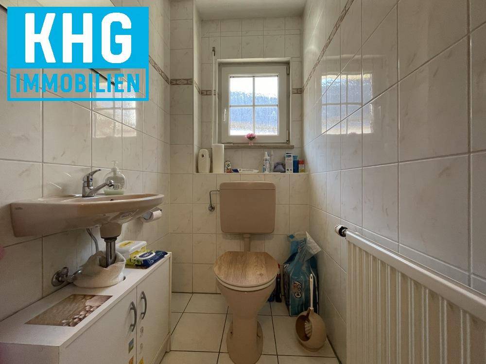 Separates WC mit Fenster, Wandfliesen und einem kleinen Waschbecken, funktional eingerichtet.