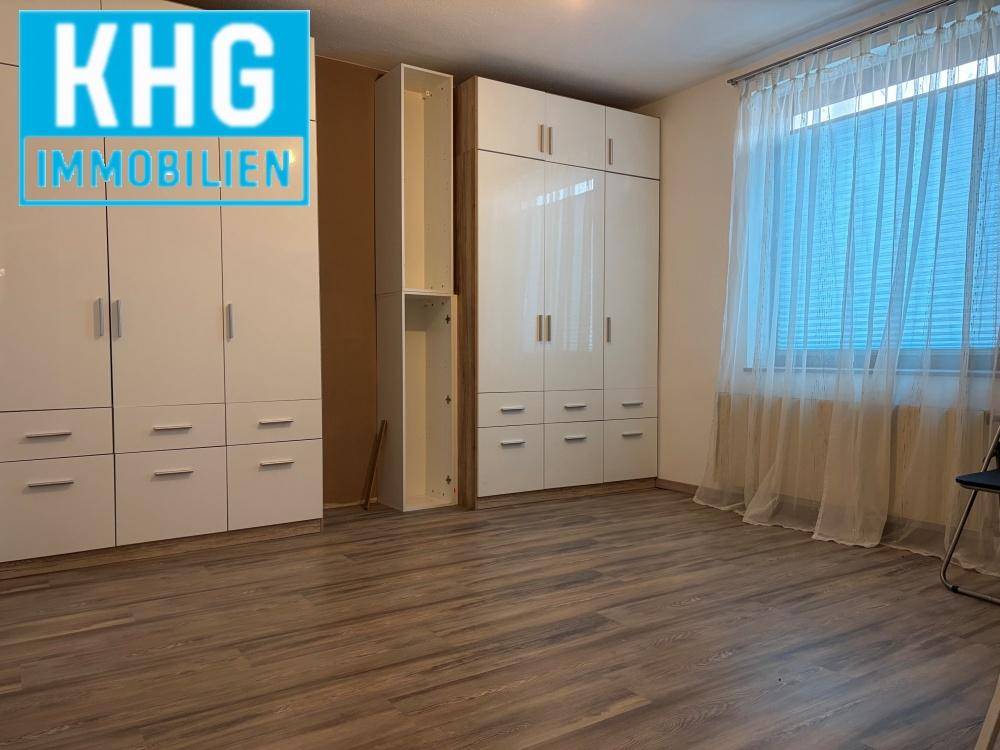 Geräumiges Schlafzimmer mit Laminatboden, großem Fenster und weißen Einbauschränken.